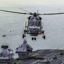 a wildcat helicopter flies above HMS Queen Elizabeth with grey waters and grey skies in background