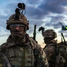 fatigue-dressed royal marine with camera placed on helmet under atmospheric interspersed cloudy skies looks into camera with fellow marine in background