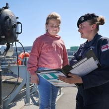 Small girl in pink sweater enjoys a day on HMS Albion while being talked to by a female officer