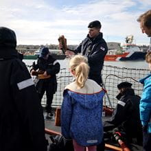 Officer onboard HMS Montrose demonstrates equipment to other officers and families