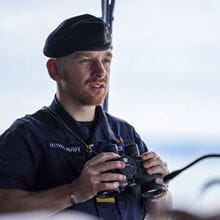 A Royal Navy sailor hold up his binoculars