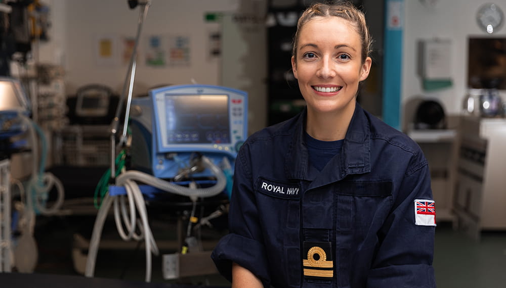 face on image of smiling blonde haired uniformed lieutenant nurse on board HMS Queen Elizabeth medical facility with clinical equipment in background