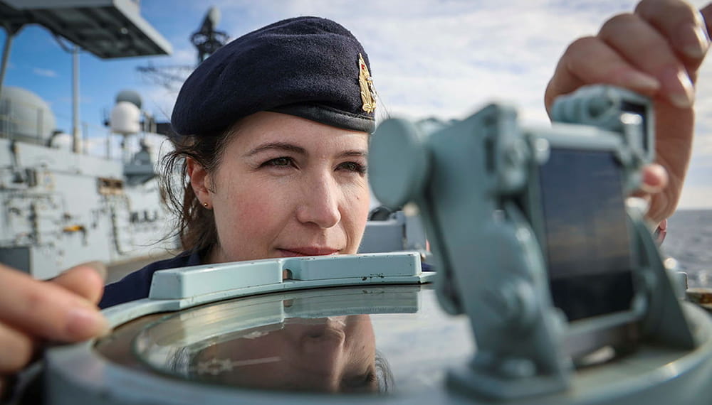 royal navy crewmember on board works with unit of navigation equipment under blue skies