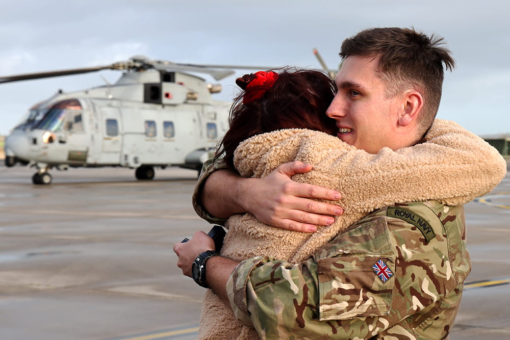 dressed in fatigues a naval air squadron member hugs a loved on an airstrip