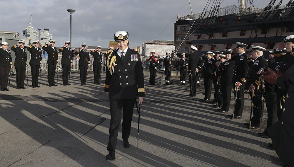 Maritime Reserves Commodore Robinson walks towards the camera surrounded by officers during the supersession ceremony