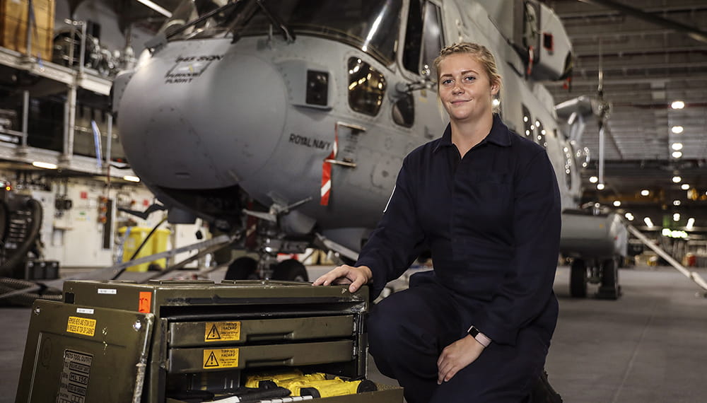 knelt down uniformed blonde haired leading Air Engineer with merlin helicopter behind on deck of HMS queen elizabeth aircraft carrier
