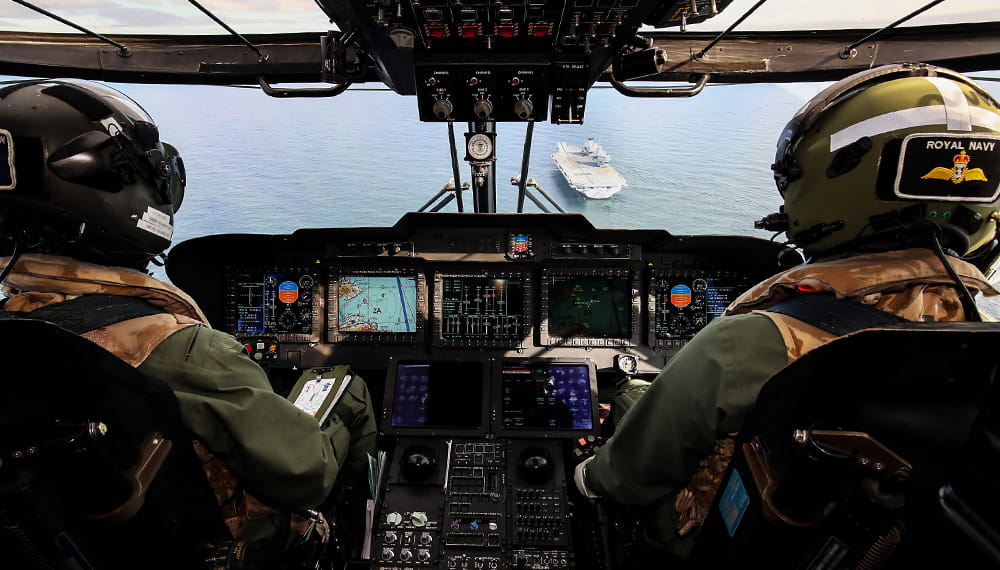 Image from behind of uniformed and helmeted pilot and navigator of a merlin helicopter crew from NAS 820 squadron approaching aircraft carrier