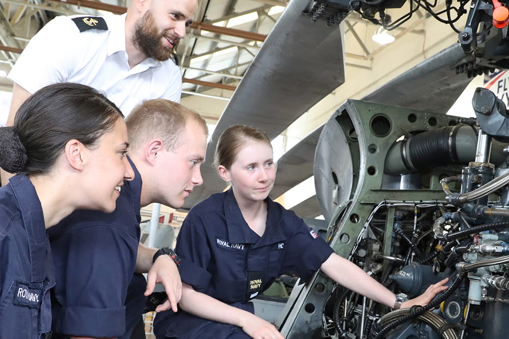 Royal Navy engineers and technicians inspect aircraft overseen by an officer