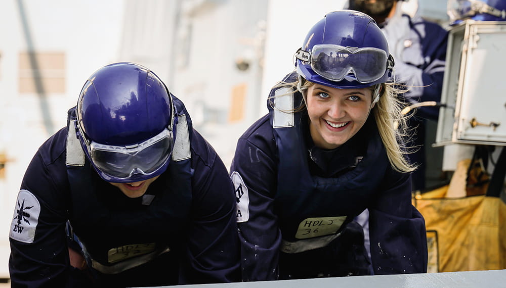 Royal Navy personnel looking towards the camera smiling during a replenishment at sea