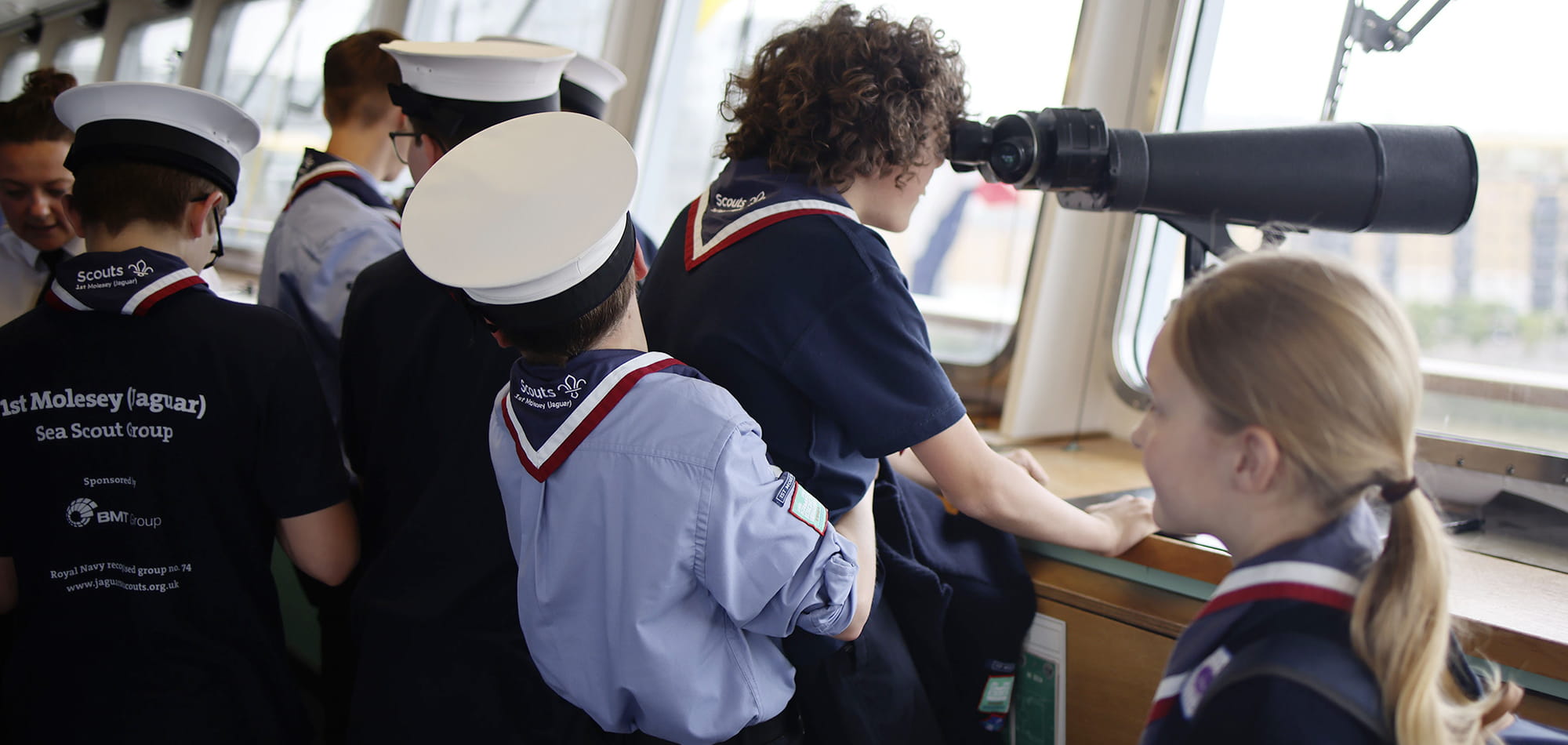 group of sea cadets on bridge of ship with one cadet looking through binoculars