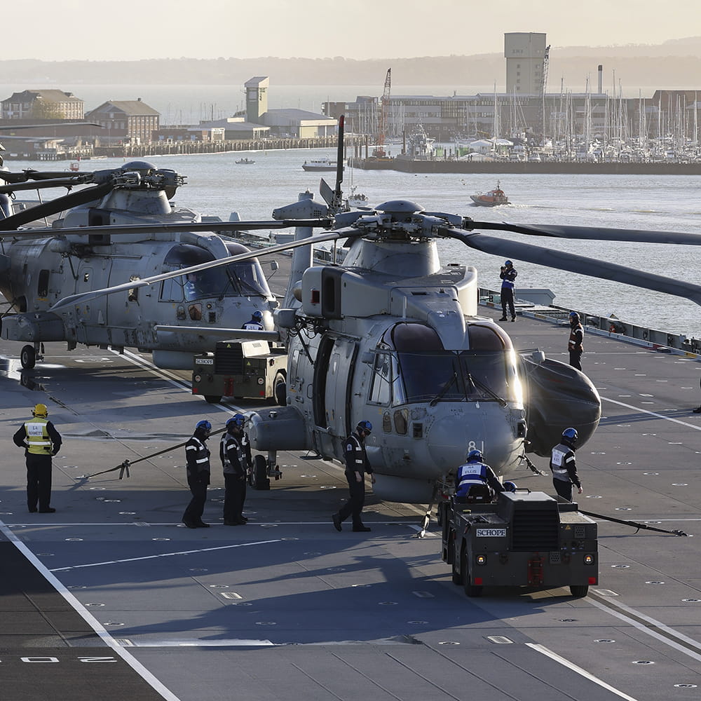 Two Merlin helicopters get loaded up on the deck of an aircraft carrier