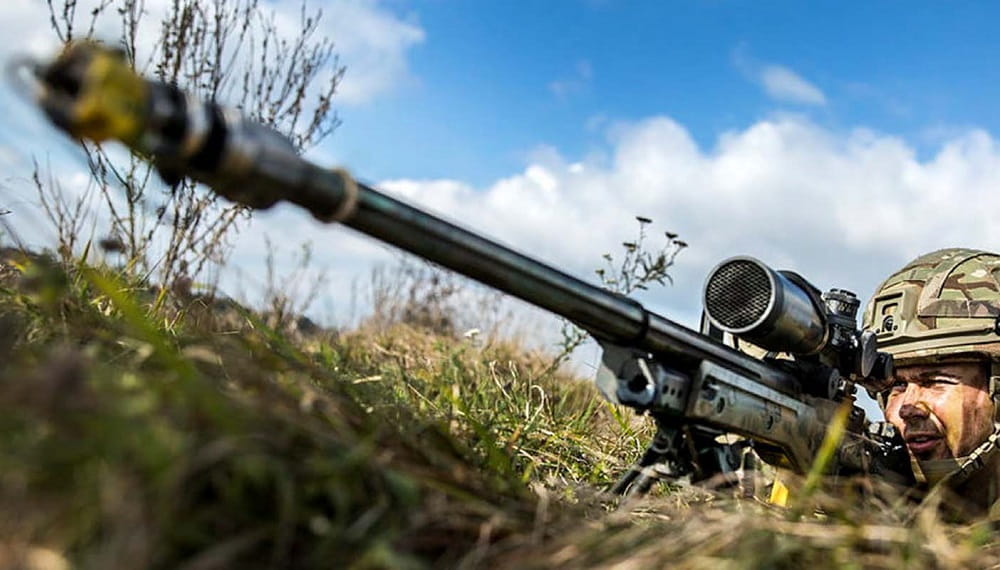 Troop aiming an L96 sniper rifle in grass
