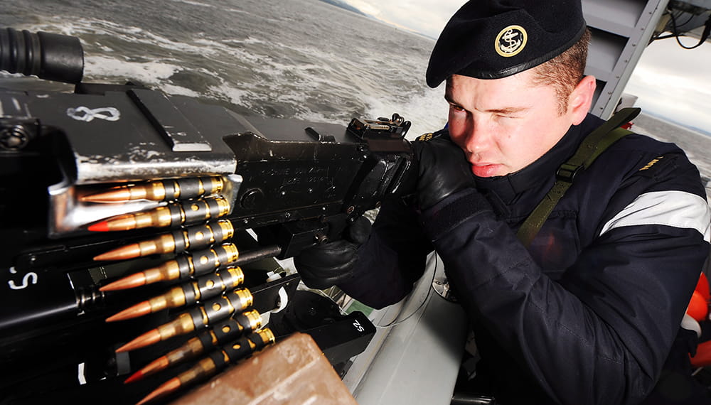 Royal Navy sailor aims a large machine gun