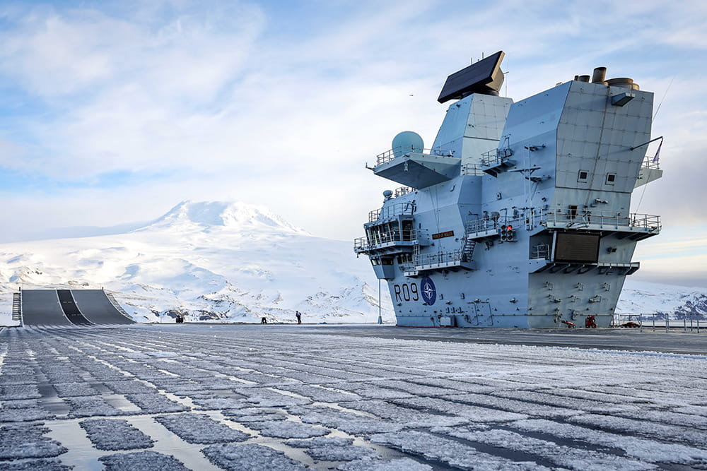 Icey deck of an aircraft carrier with a snow-covered mountain in the distance
