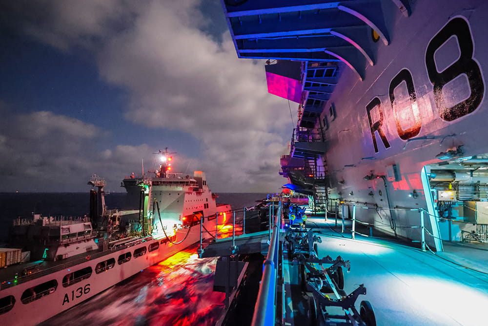 Pink, orange and blue lights light up the deck of the HMS Queen Elizabeth while being refueled by RFA Tidespring