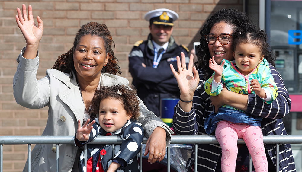 Two women and children waving with a Navy officer in background