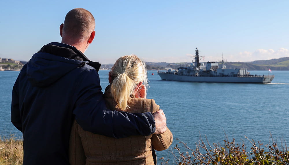 Man and woman with back to camera watching HMS Montrose sail away