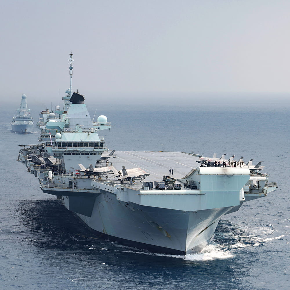 HMS Queen Elizabeth and HMS Defender lined in open waters