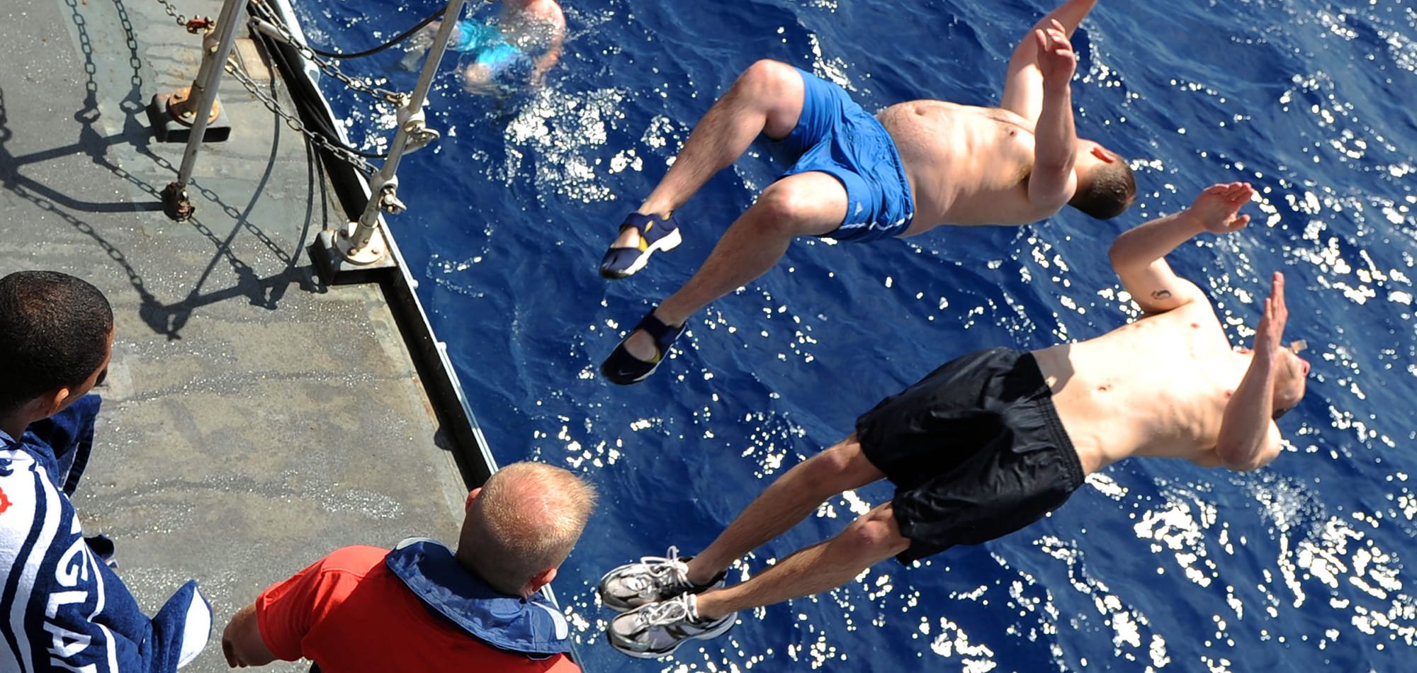A couple of persons do a backflip into the sea off the HMS St Albans during the Hands To Bathe