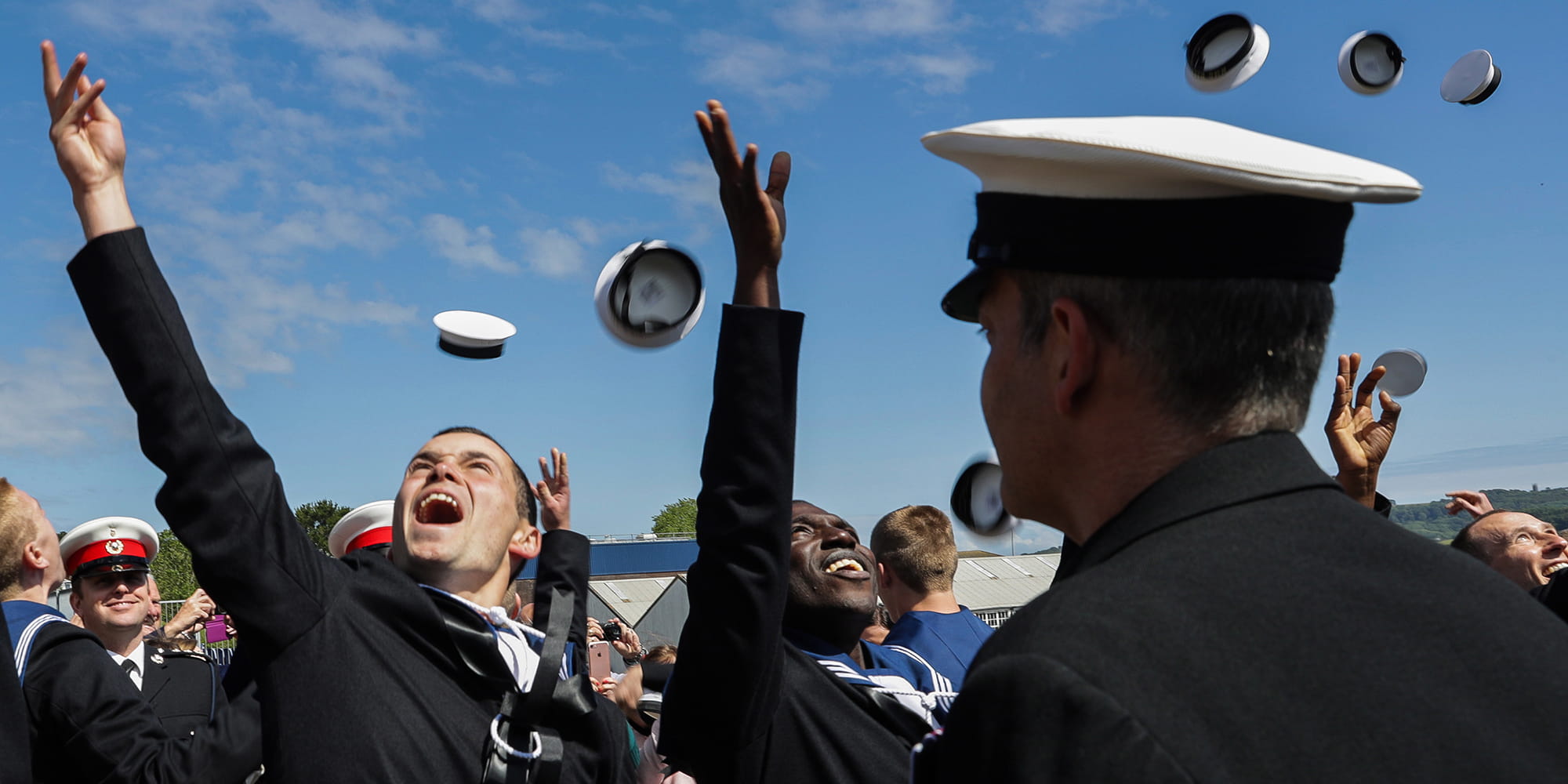 Trainee sailors celebrating at passing out parade throwing their hats in the air