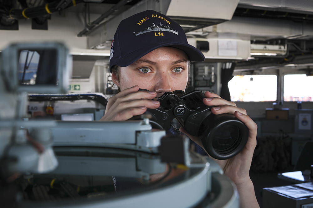 A Royal Navy Officer makes a navigation check with her binoculars