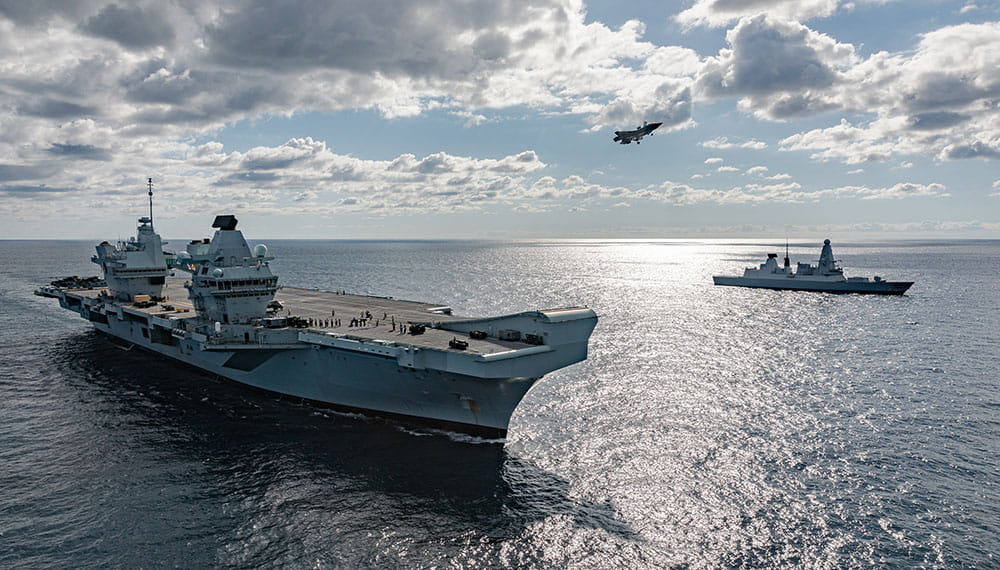 Fighter Jet coming in to land on HMS Queen Elizabeth Aircraft Carrier with Type 45 frigate in background