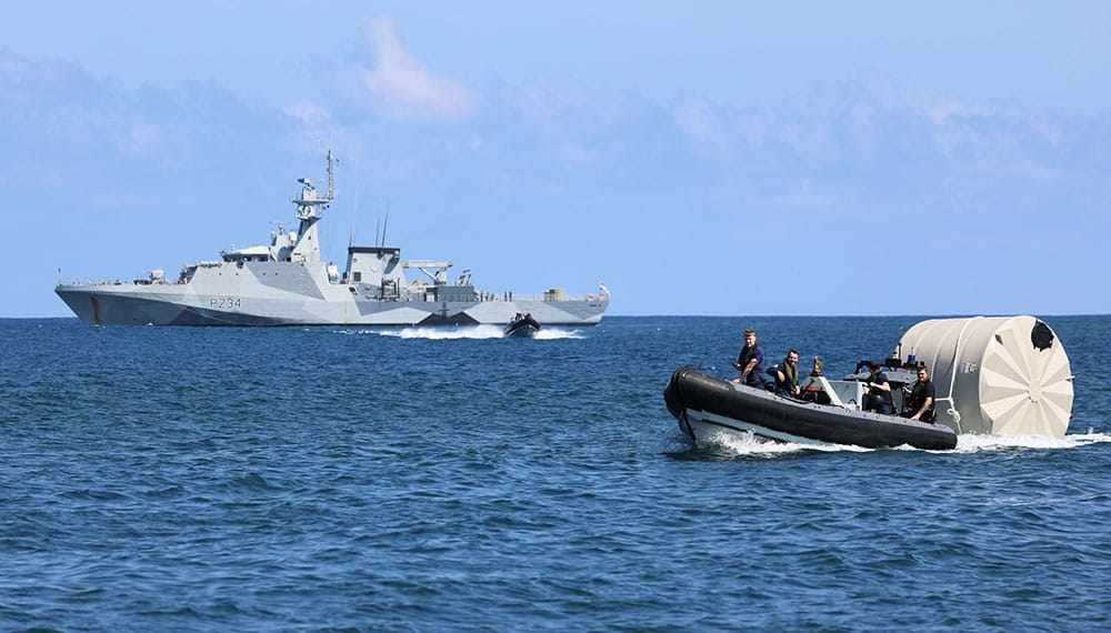 HMS Spey in background delivers humanitarian aid via small inflatable vessel in forground 