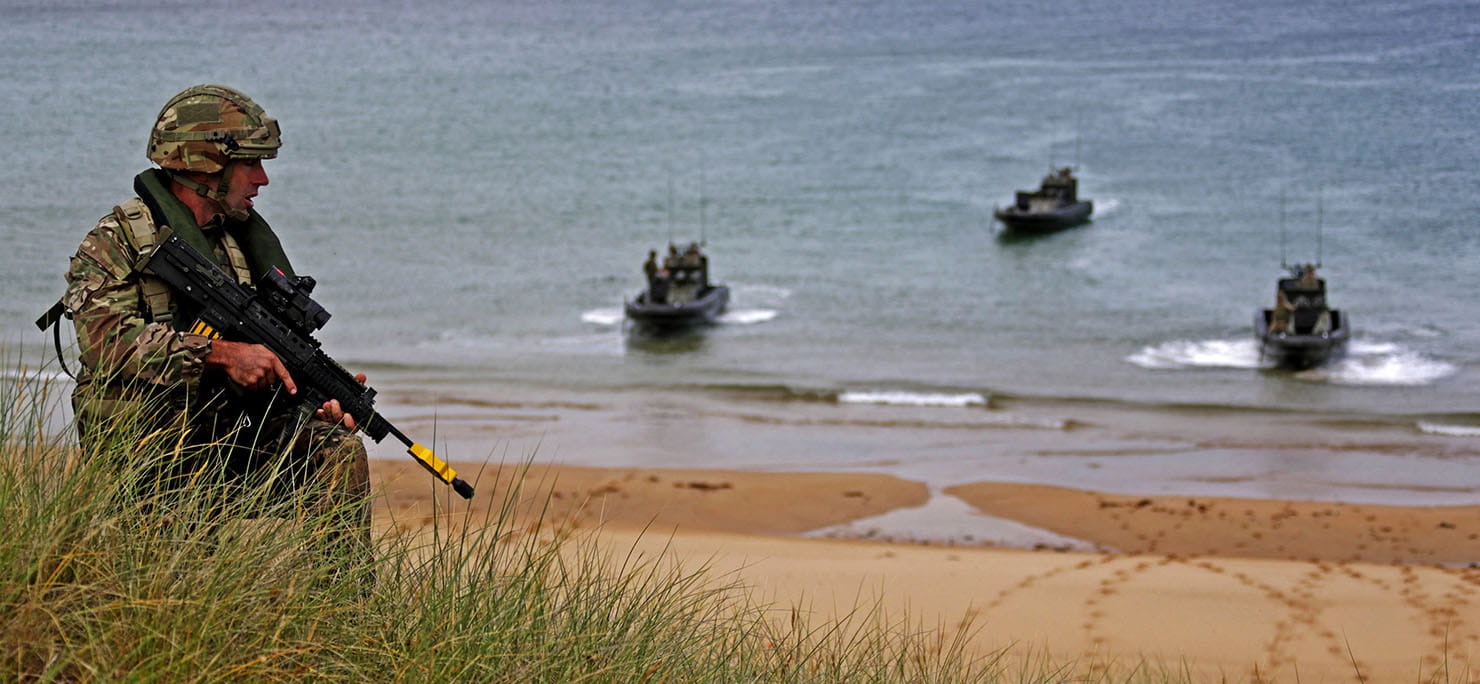 A Royal Marine making his way up a beach head at Castle Martin range while ORCs provide covering fire from the sea