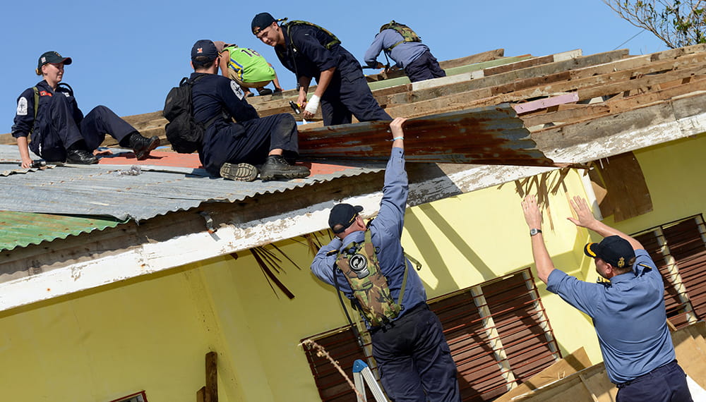 Royal Navy sailors fix a corrugated iron roof